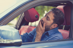 sleepy fatigued yawning exhausted young man driving his car in traffic after long hour drive